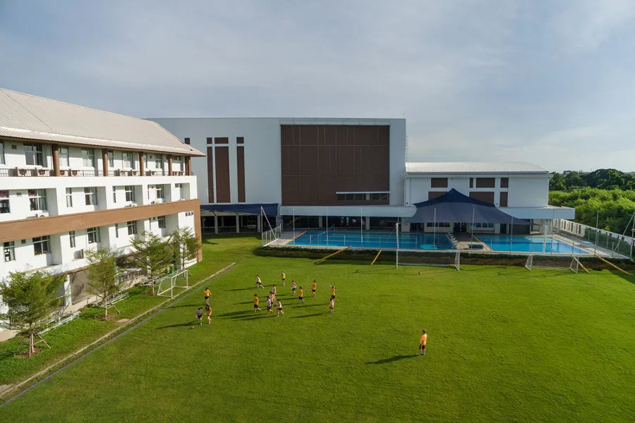 ภาพถ่ายทางอากาศของบริเวณโรงเรียนที่มีอาคารขนาดใหญ่สองหลัง สนามฟุตบอล นักเรียนกำลังเล