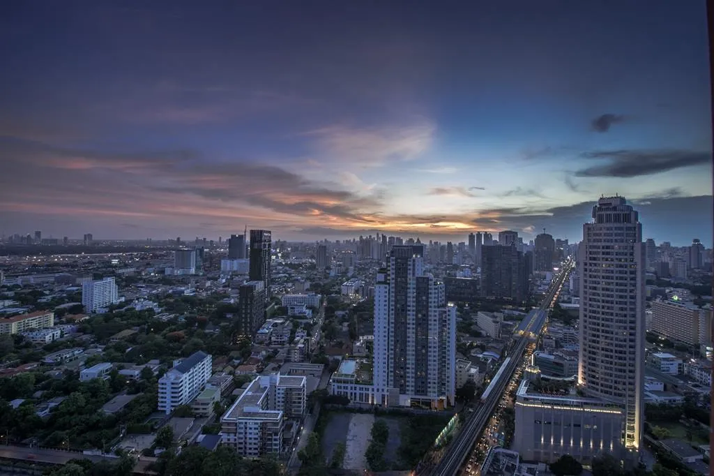 ภาพถ่ายทางอากาศของเส้นขอบฟ้าเมืองยามพลบค่ำ แสดงให้เห็นตึกสูง ถนนที่สว่างไสวด้วยแสงไฟ 