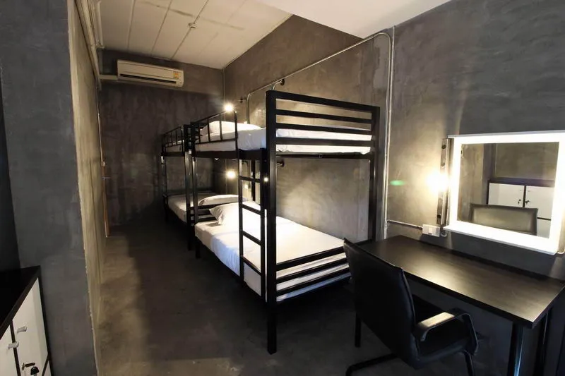 A minimalist room with two sets of metal bunk beds, a desk with a chair, and a wall-mounted mirror.