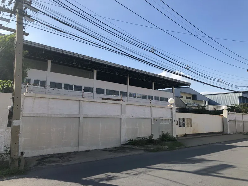 Large industrial building with a white exterior wall and barbed wire, set against a clear blue sky, with overhead power lines in the foreground.