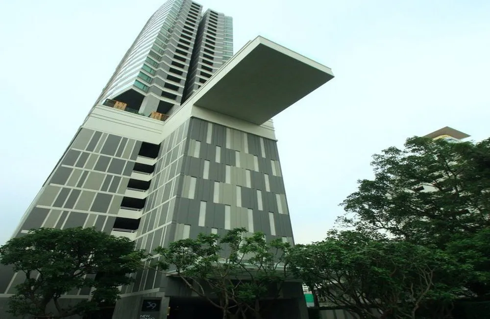 Tall modern skyscraper with geometric facade, angled perspective, surrounded by trees against a clear sky.