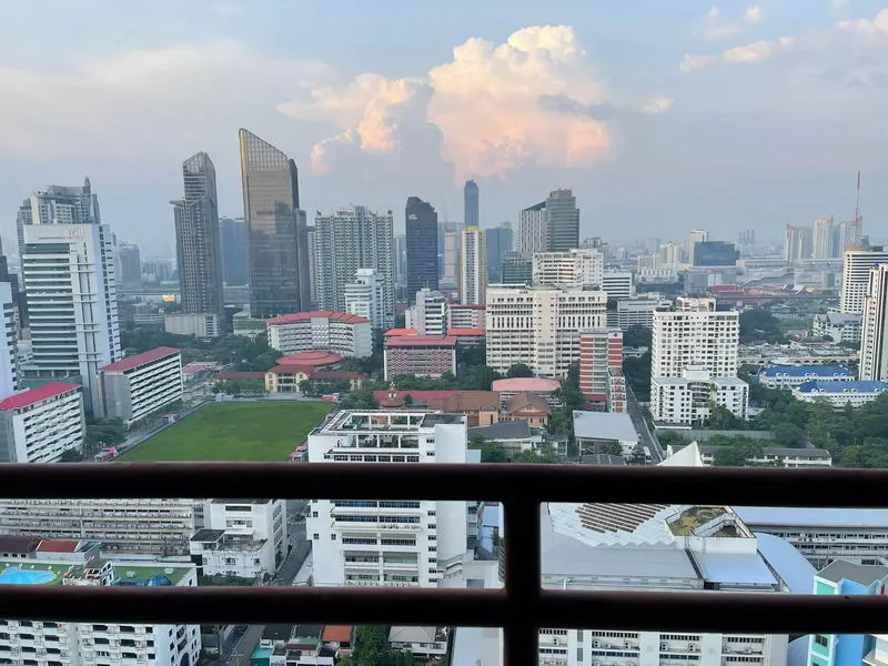 View of a city skyline with modern high-rise buildings, a lush green park in the foreground, and pink clouds in the background.