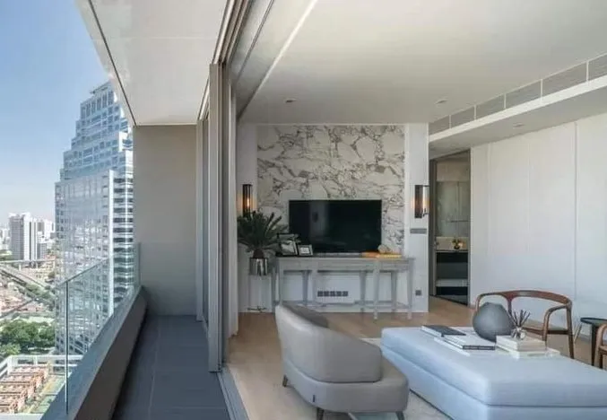 Modern living room with marble accent wall, TV, light blue ottoman, and large windows overlooking a city skyline.