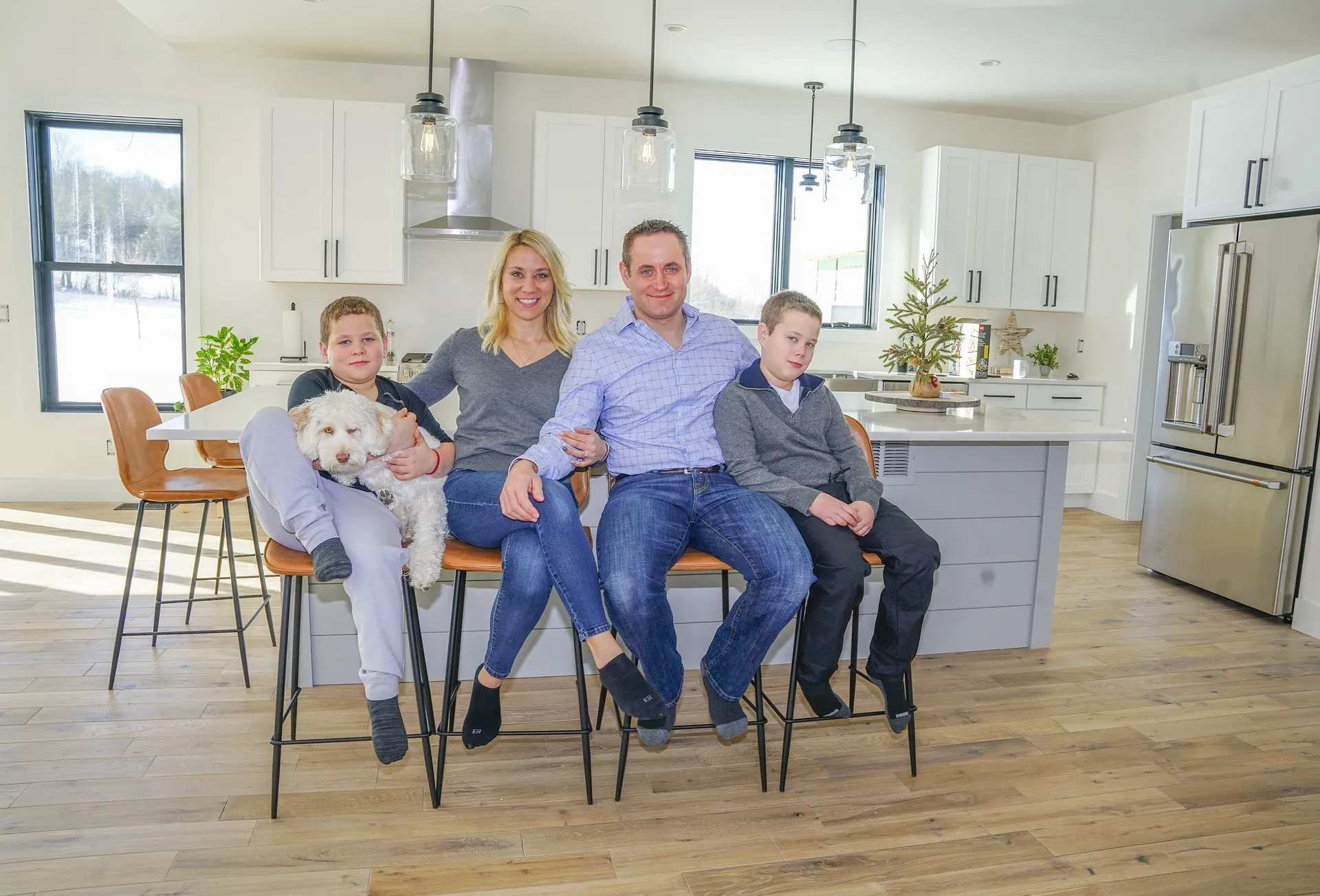 一家人坐在现代化的厨房里，厨房里有白色橱柜、吊灯，一只小狗坐在椅子上。