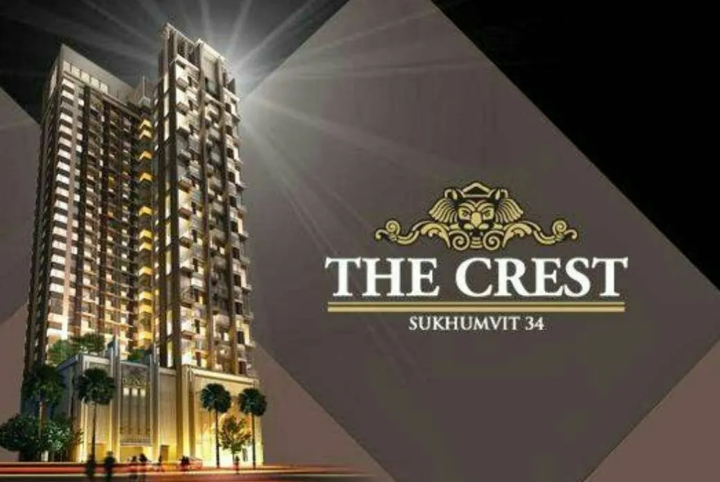 อาคารสูงที่ส่องสว่างด้วยไฟ มีโลโก้ "The Crest Sukhumvit 34" บนพื้นหลังสีเข้ม โดยมีต้นปาล์มอยู่บริเ