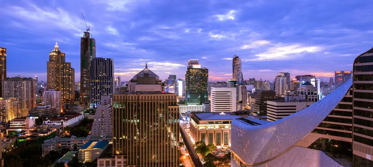 ภาพทิวทัศน์เมืองยามพลบค่ำ ตึกระฟ้าทันสมัยส่องสว่างภายใต้ท้องฟ้าสีน้ำเงินและม่วงสดใส