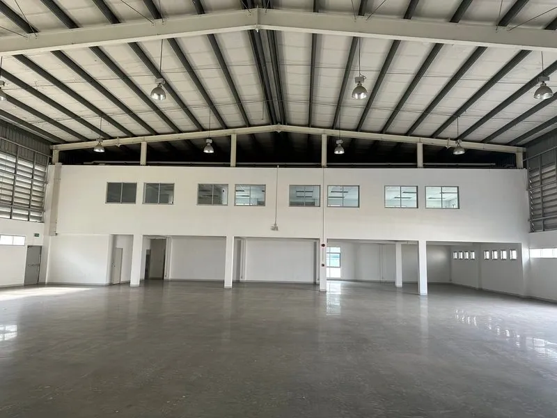 Spacious empty warehouse interior with high ceiling, overhead lights, large doors, and windows.