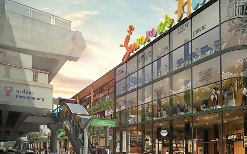 Skytrain station next to a colorful modern shopping center with large glass windows showcasing various storefronts and signs.