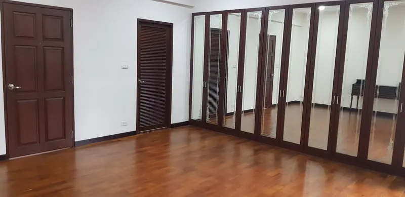 Spacious empty room with wooden floor, two brown doors, and a large mirrored wardrobe on one wall.