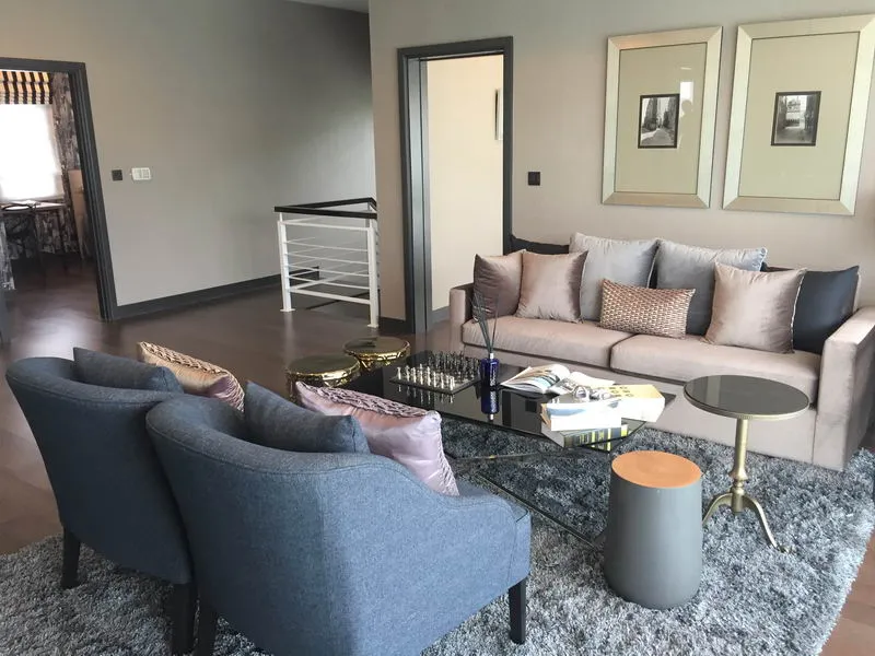 Modern living room with gray sofa, blue armchairs, a glass coffee table with books, a chessboard, and abstract wall art.