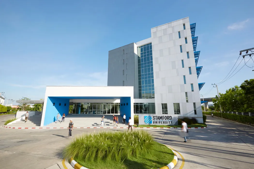 อาคารมหาวิทยาลัยสมัยใหม่ที่มีภายนอกสีขาวและสีฟ้า หน้าต่างกระจก และผู้คนกำลังเดินเล่น