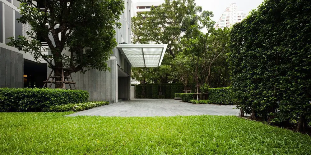 Modern building entrance with surrounding lush greenery and a well-maintained lawn.