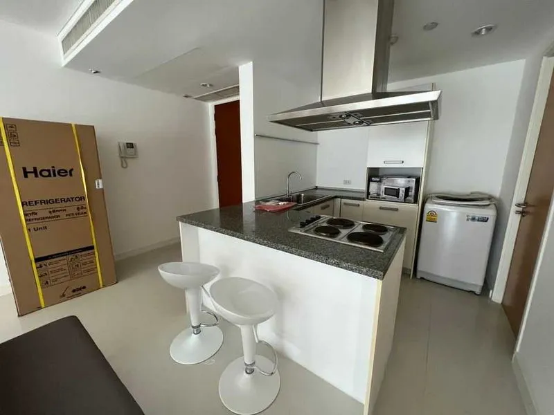 Modern kitchen with an island, bar stools, stove, sink, microwave, washing machine, and a boxed refrigerator.
