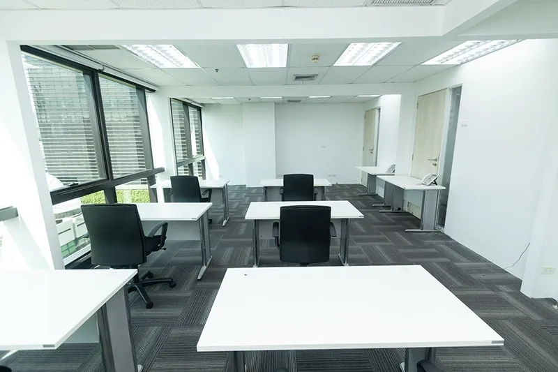 Modern office with white desks, black chairs, large windows, and gray carpet tiles.