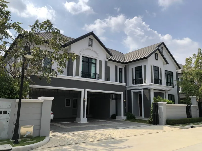 Two-story modern house with gray and white exterior, large windows, and a manicured front yard under a partly cloudy sky.