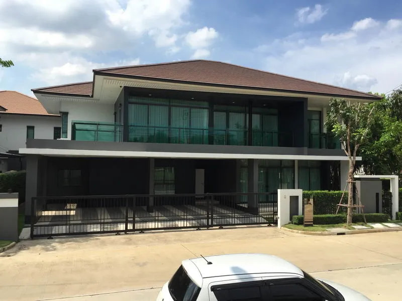 บ้านสองชั้นสไตล์โมเดิร์น หลังคาแบน หน้าต่างบานใหญ่ และทางเข้าบ้านมีรั้วกั้น ท่ามกลางท้