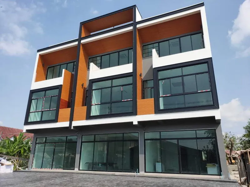 Modern three-story building with large glass windows, geometric design, and wood accents, set against a blue sky.