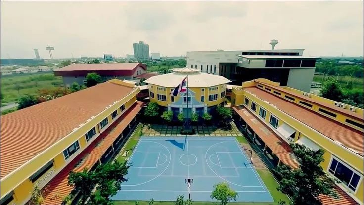 ภาพถ่ายทางอากาศของกลุ่มอาคารเรียนที่มีหลังคาสีเหลืองล้อมรอบสนามบาสเก็ตบอลสีฟ้า โดยมี