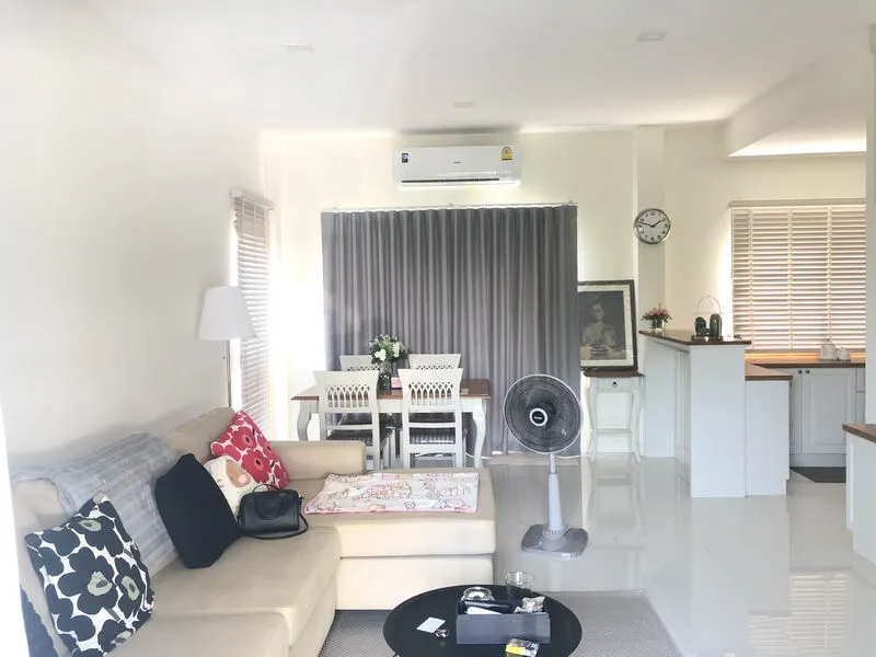 Living room with a beige sofa, dining table, stand fan, lamp, and wall clock, featuring gray curtains and an air conditioner.