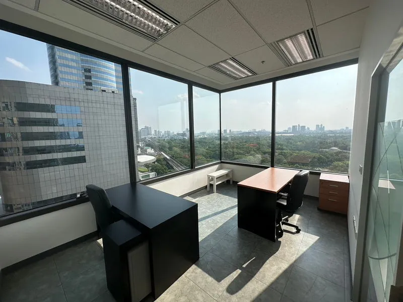A modern office with natural light, featuring two desks, chairs, and a panoramic city view from corner windows.