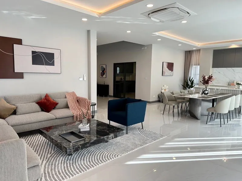 Modern open-concept living and dining area with a gray sofa, blue chair, marble coffee table, abstract wall art, and a dining table with eight chairs.