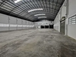 Inside view of a large, empty warehouse with a high arched ceiling, concrete floor, and several small windows along the walls.