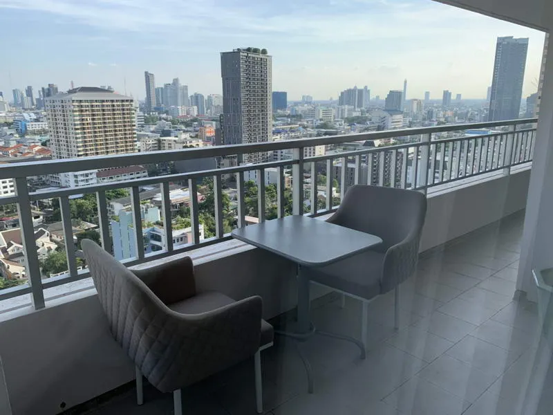 Balcony view with two chairs and a table overlooking a cityscape with tall buildings under a clear sky.