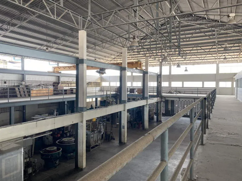 Industrial warehouse interior with high ceilings, metal railings, and machinery.