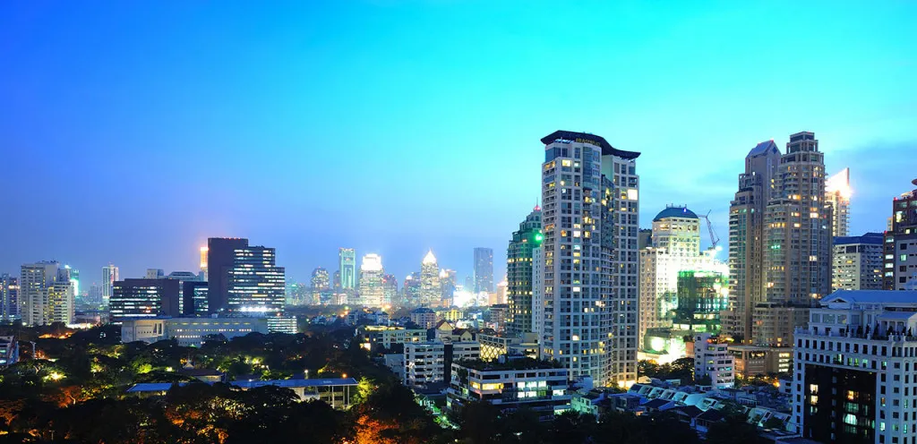 Evening cityscape with a skyline of tall buildings lit against a blue sky.