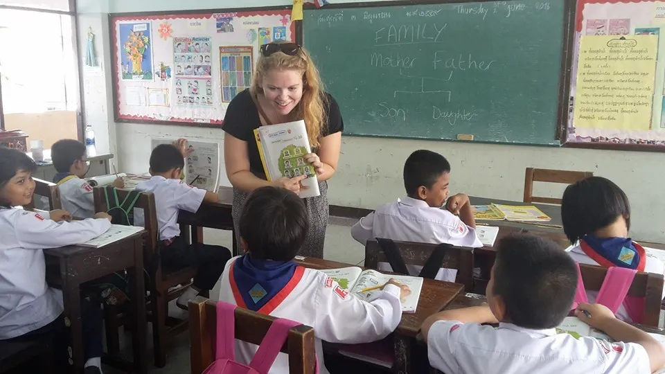 ครูมีปฏิสัมพันธ์กับนักเรียนในห้องเรียน โดยถือหนังสือไว้ ขณะที่เด็กๆ ในชุดนักเรียนกำลั