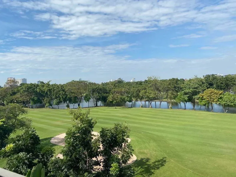 A golf course with neatly mowed grass, surrounded by trees and a river under a blue sky with scattered clouds.