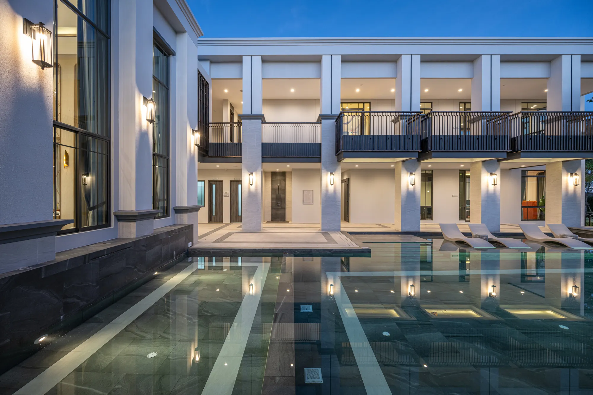 Modern luxury villa exterior at twilight with a reflecting pool in the foreground and sleek architecture with large windows and elegant lighting.