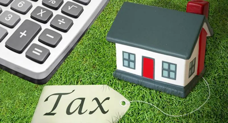 เครื่องคิดเลข บ้านของเล่น และป้ายที่มีข้อความว่า "ภาษี" วางอยู่บนสนามหญ้าสีเขียว สื่