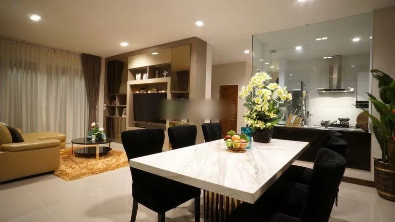 Modern living and dining area with marble table, black chairs, leather sofa, and open kitchen.