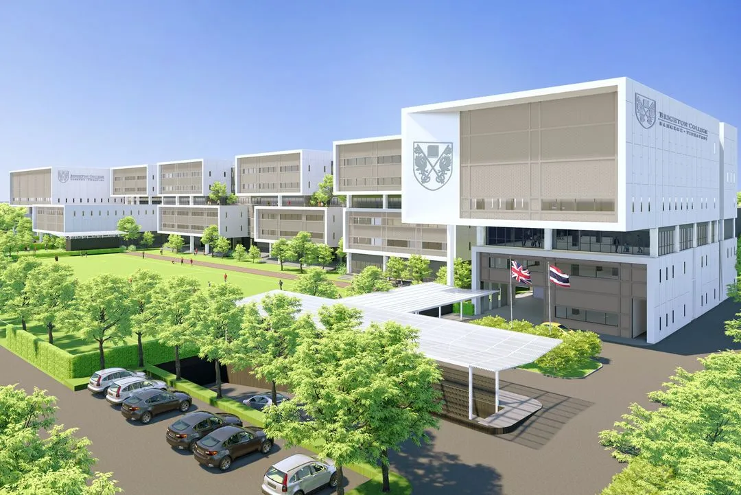 อาคารเรียนสมัยใหม่หลายชั้น มีสนามหญ้าหน้าบ้านขนาดใหญ่ ต้นไม้ รถยนต์จอดอยู่ และมีธงสองผ