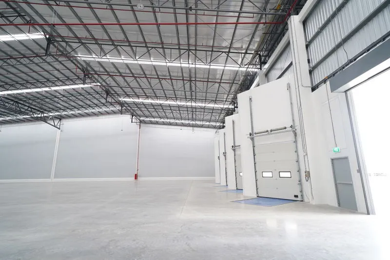 Empty warehouse interior with high ceilings, loading bay doors, and polished concrete floors.