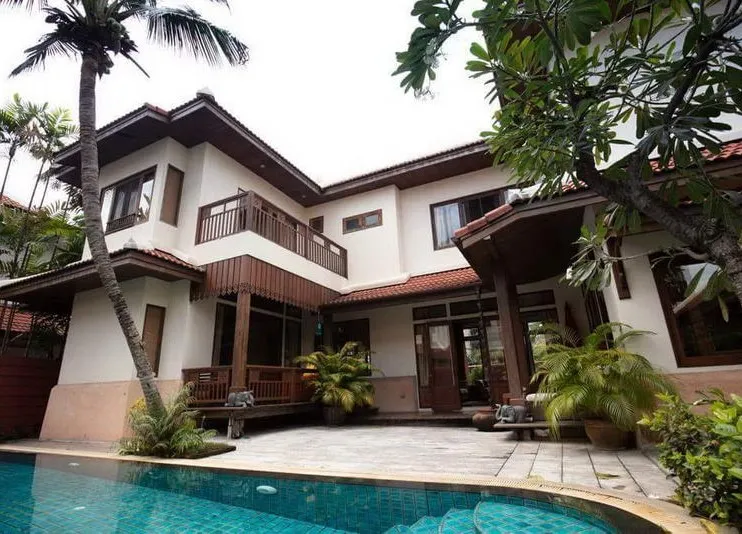 Two-story house with tropical plants and an outdoor patio beside a swimming pool.