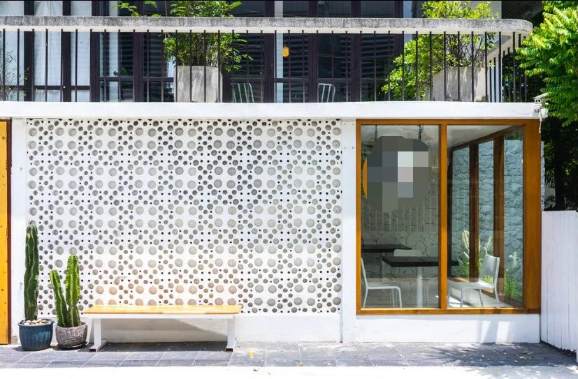 Modern building facade with circular patterned wall, glass windows, a wooden bench, and potted cacti.