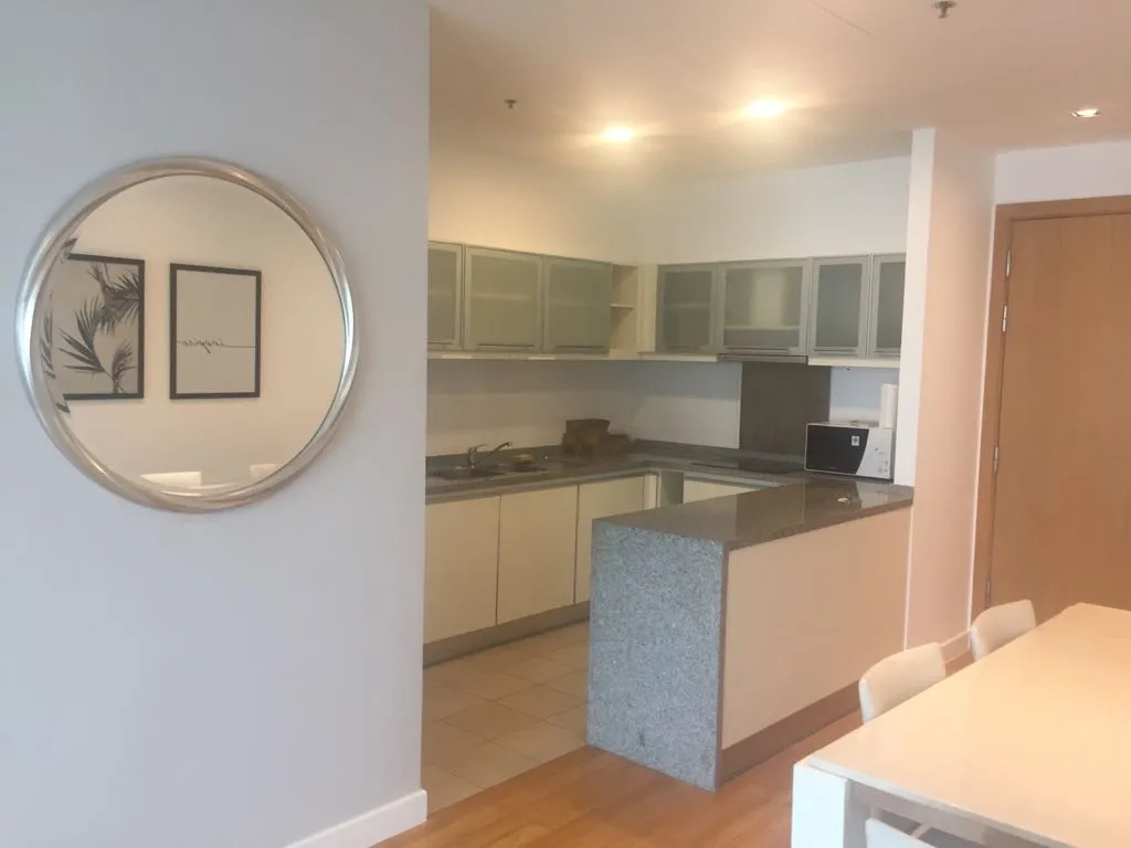 Modern kitchen with white cabinets, gray countertops, and a round mirror reflecting framed artwork.
