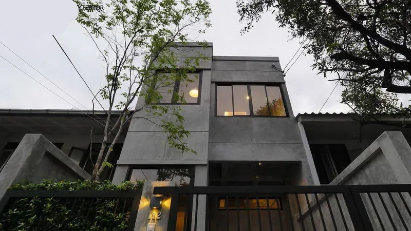 A modern two-story house with large windows and a concrete exterior, surrounded by trees, viewed from the street.