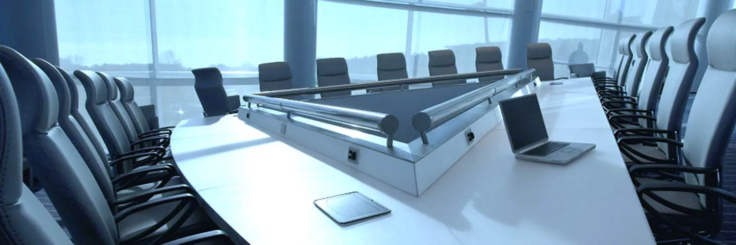 ห้องประชุมขนาดใหญ่ มีโต๊ะสีขาวทรงสามเหลี่ยมล้อมรอบด้วยเก้าอี้สีดำและสีขาว และมีแล็ปท
