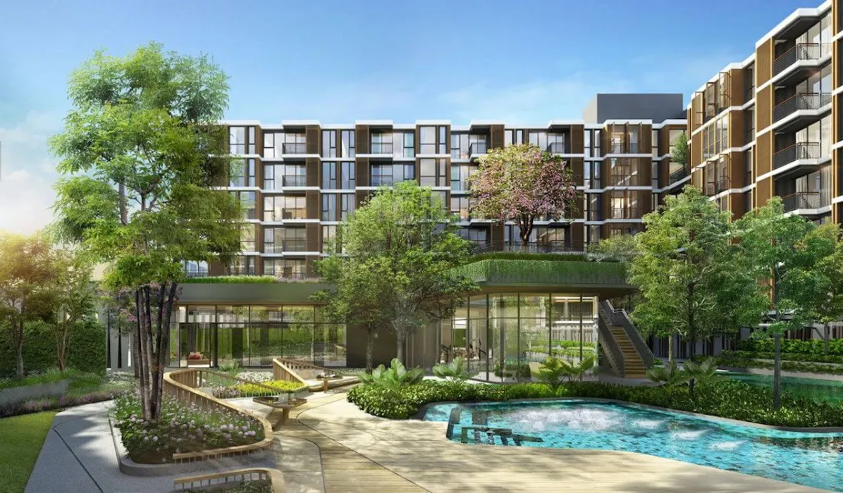 Modern apartment building with glass windows, surrounded by landscaped gardens and trees, featuring an outdoor pool under a clear blue sky.