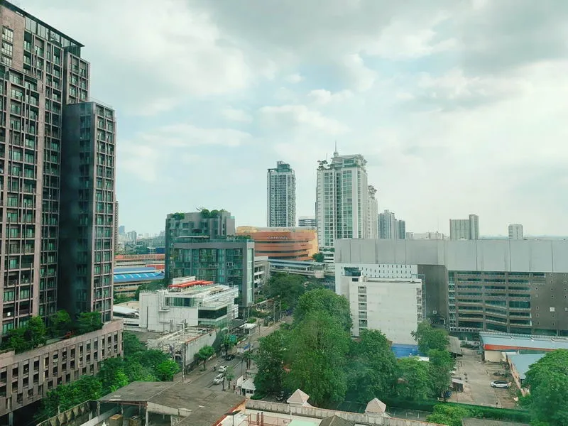Cityscape with high-rise buildings, greenery, and cloudy sky.