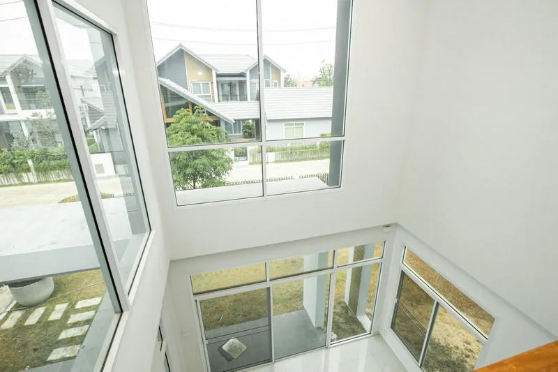 Interior view of a modern house with large windows overlooking neighboring homes and a small garden.