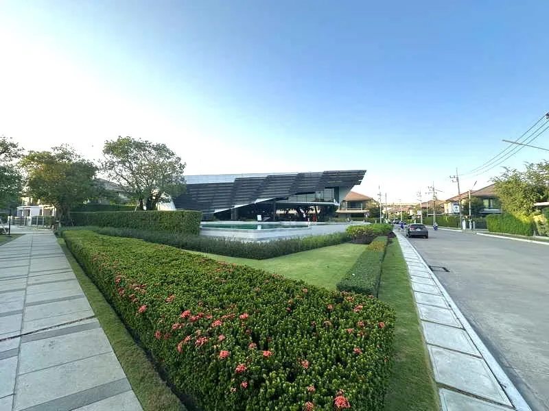 Modern building with a distinctive roof design, surrounded by well-maintained hedges and flowers along a concrete walkway, under a clear blue sky.