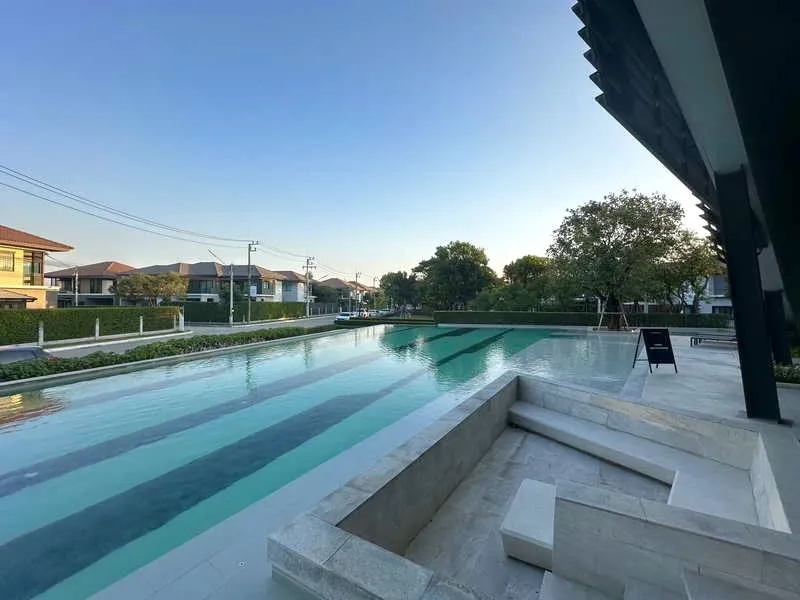 Outdoor swimming pool next to residential area, with clear sky and trees in the background.