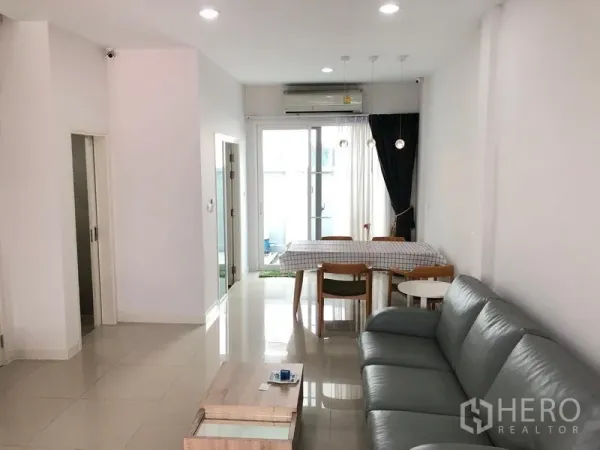 联排别墅 出租或出售在Wang Thonglang, Bangkok - 明亮的客餐厅一体空间，灰色沙发、瓷砖地面与落地推拉玻璃门。