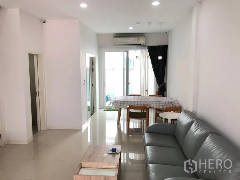 联排别墅 出租或出售在Wang Thonglang, Bangkok - 明亮的客餐厅一体空间，灰色沙发、瓷砖地面与落地推拉玻璃门。