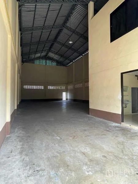 Warehouse for rent in Bang Bua Thong, Nonthaburi - High-ceiling warehouse interior with steel truss roof and polished concrete floor, view toward rear exit.