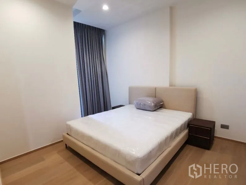 公寓 出租在Bang Rak, Bangkok - 卧室配软包大床、床头柜与遮光窗帘，空间简洁明亮。